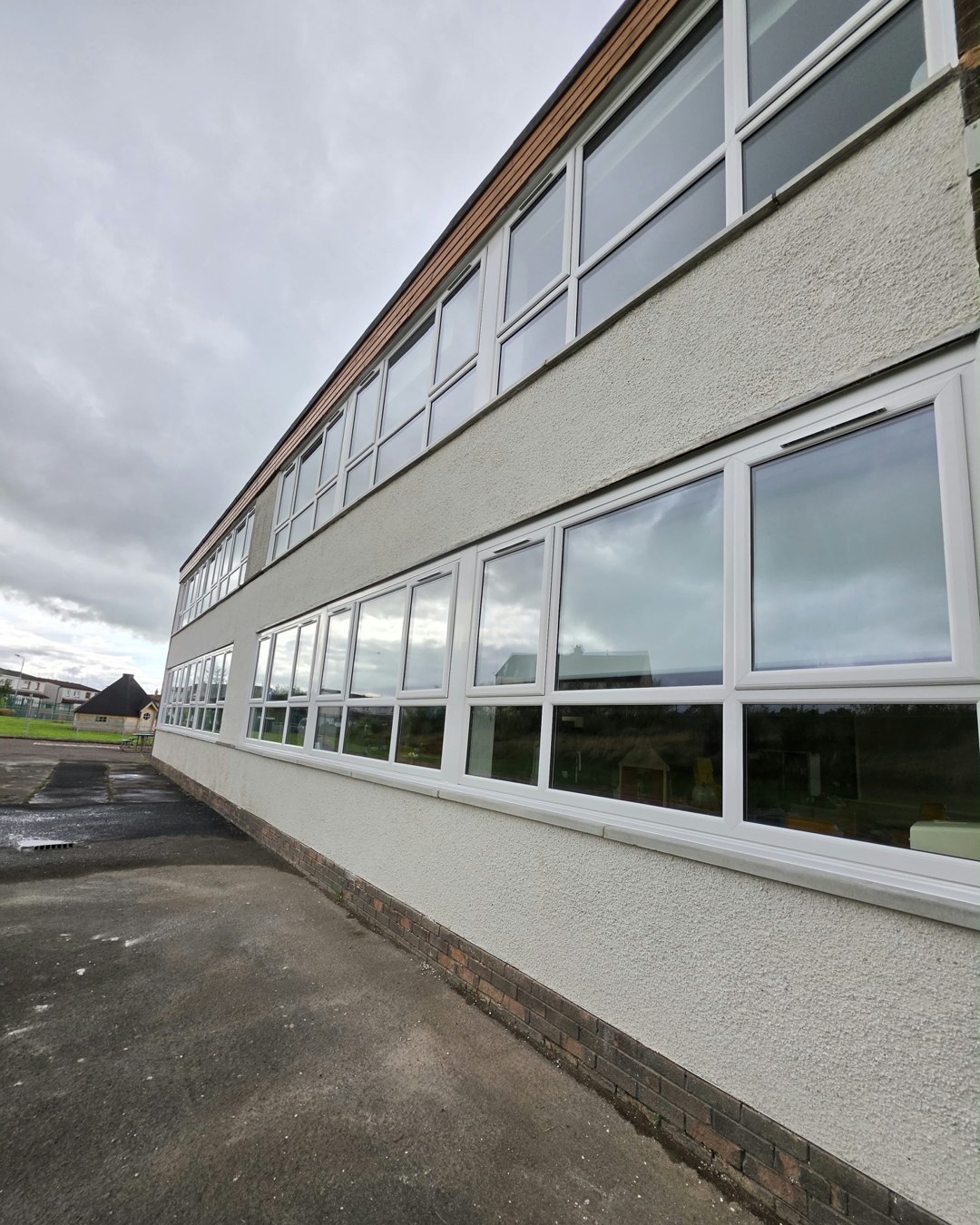 The long two-storey classroom block at Logan Primary School, with new white VEKA windows along both floors and fresh render